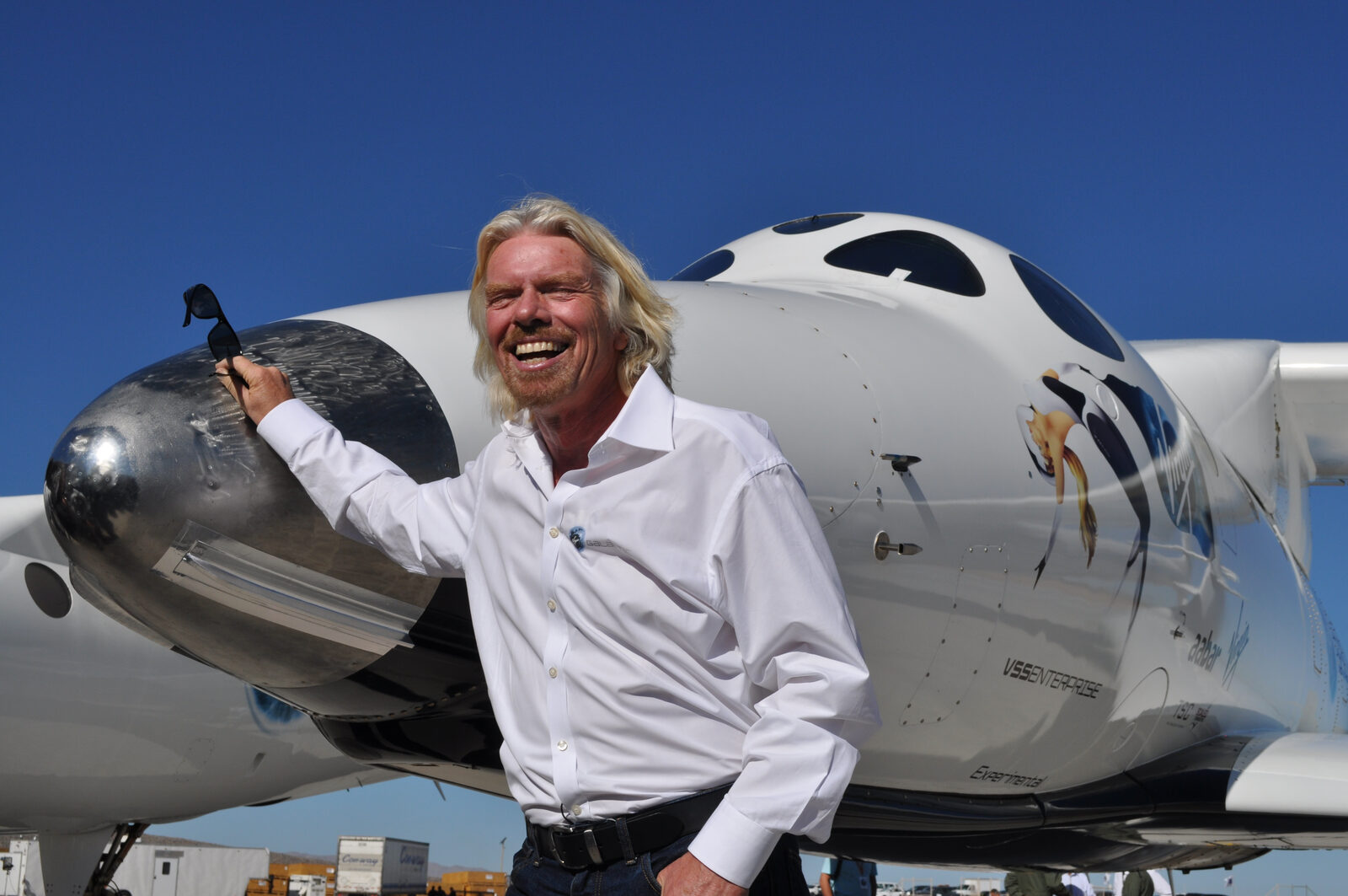 Richard Branson smiling in front of a Virgin Galactic spaceplane