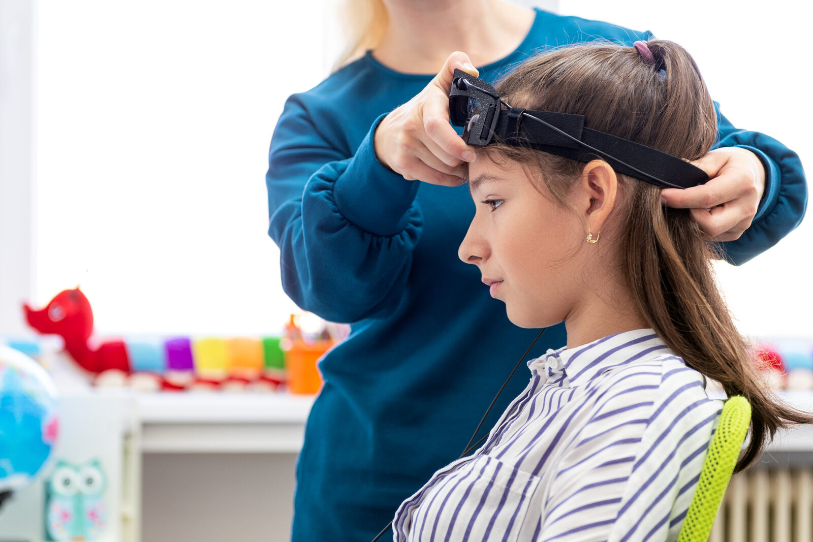 A specialist gently fits a sensor headband to a girl during an attention activity