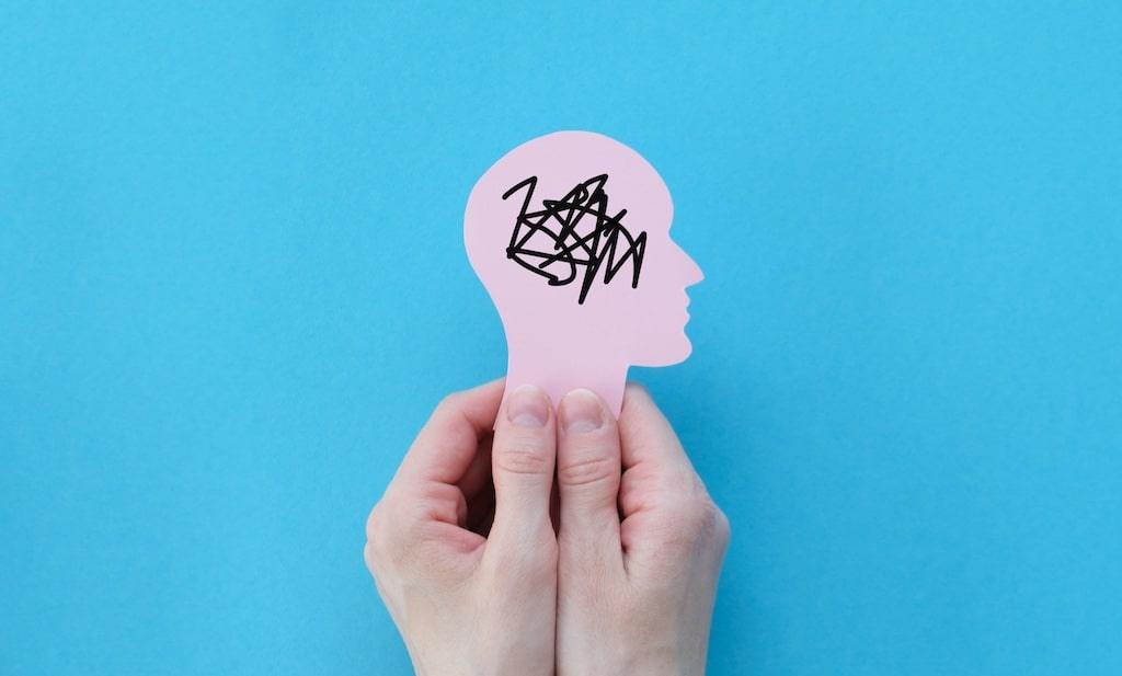 A hand holds up a paper cut-out of a head with a tangle of scribbled lines inside it